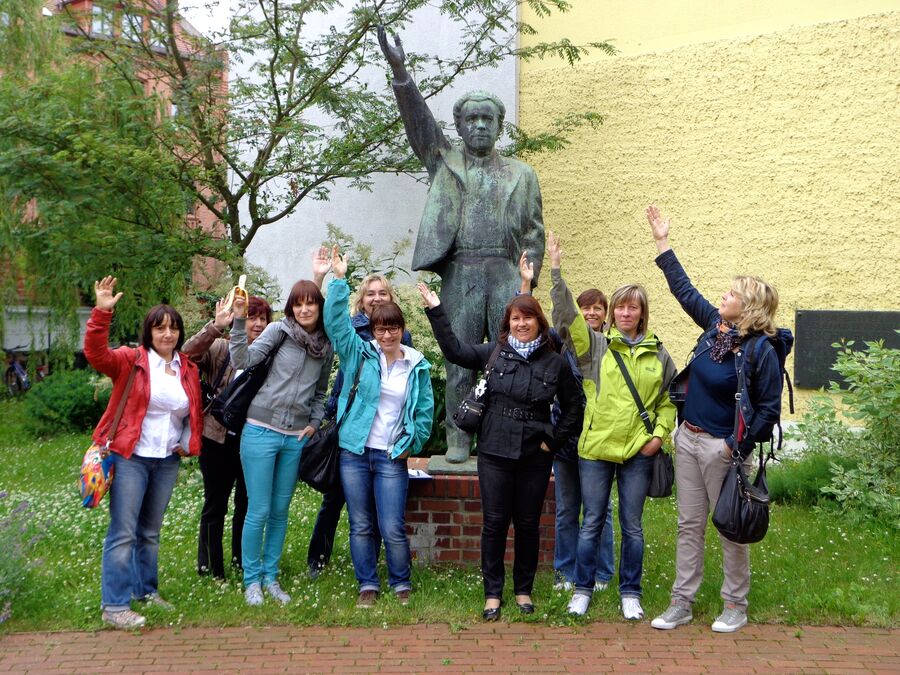 Gruppe winkt vor einem Denkmal in einer Grünanlage