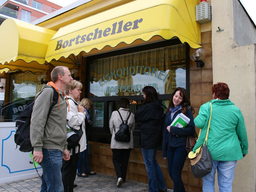 Gruppe vor einer Konditorei mit gelber Markise während einer Tour