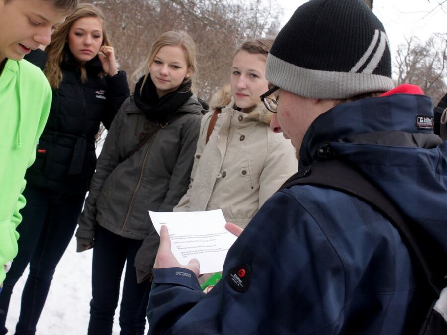 Schülergruppe mit Arbeitsblatt bei einer Geocaching-Tour im Winter